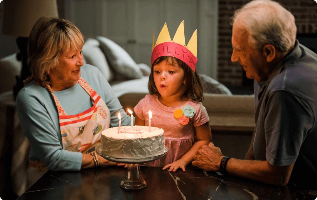 Grandparents watching their granddaughter blow out the candles on her birthday cake