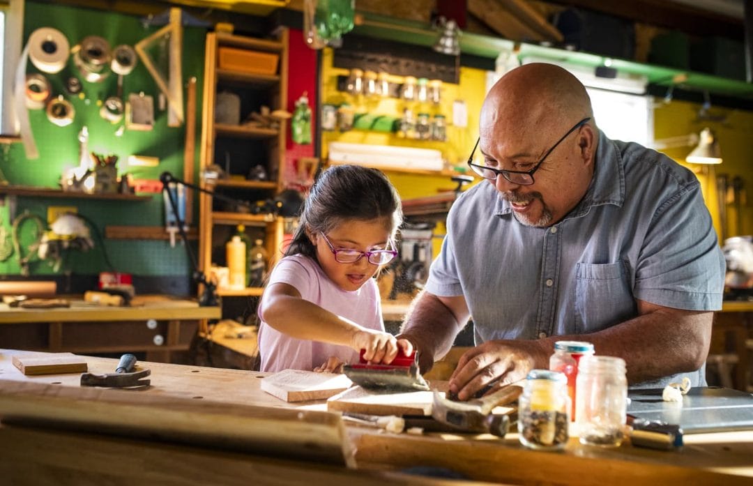 A dad and daughter sanding a birdhouse they are building